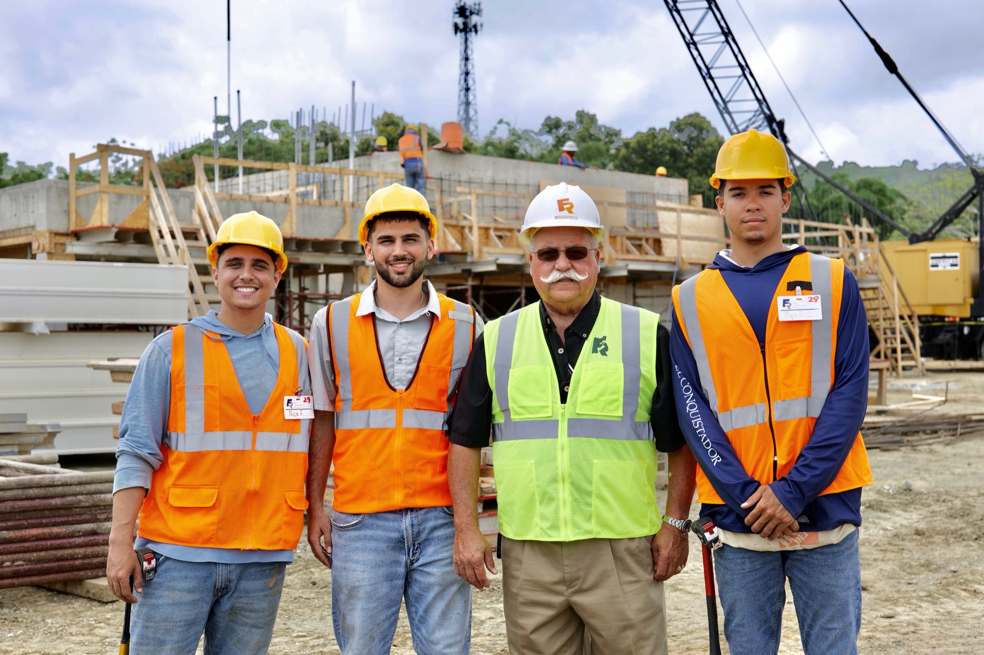Three young F&R workers in safety vests and hard hats standing with a senior site superintendent on an active F&R construction site.